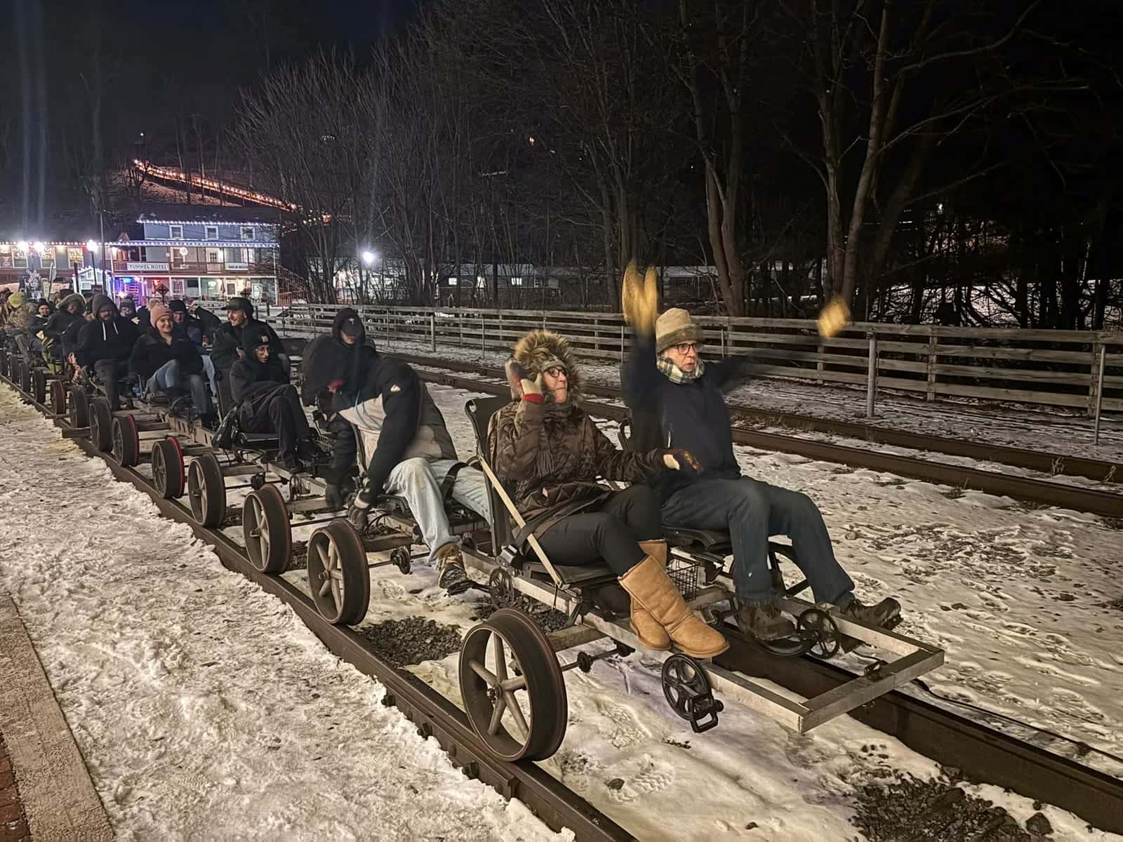 Riders on railbikes at the Frostburg Depot at night with The Tunnel Hotel lit up behind them during the Christmas Light Delight