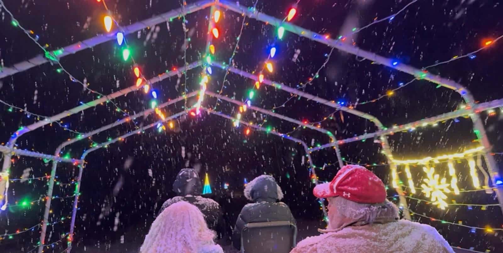 Riders in hats and hoods under a snowy arch of Christmas lights on the Mountain Christmas Light Delight railbike ride